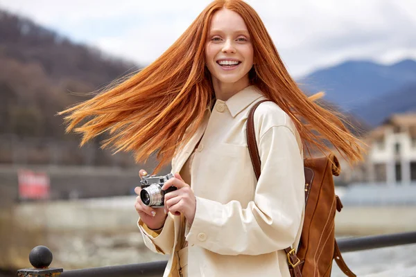 Glad rödhårig kvinna ler glad med hjälp av vintage kamera promenader på berg — Stockfoto