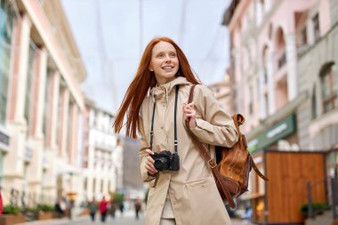 Bej ceketli, retro film kamerasıyla fotoğraf çeken mutlu bir kadın.