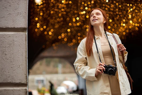 Ganska trendig ung rödhårig kvinna med kamera promenad i staden, boce i bakgrunden — Stockfoto