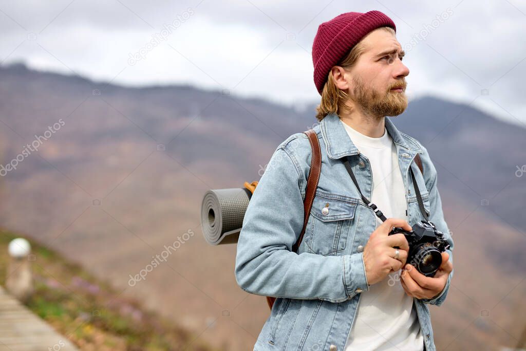 Young Caucasian man with backpack and camera is walking towards distant mountain