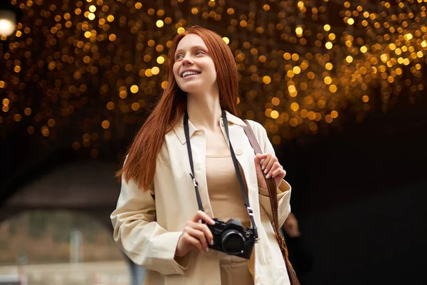 Glad resenär kvinna står utomhus på plats dekorerad med ljus, använder retrokamera — Stockfoto