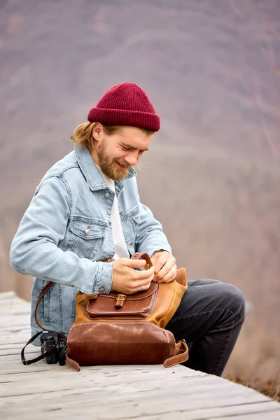 Turist man söker saker i läder brun ryggsäck under vandringen i bergen. — Stockfoto