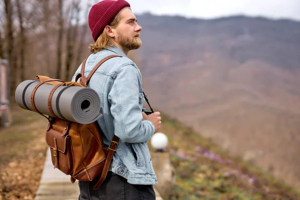 Stilig ung stilig man i jeansjacka med ryggsäck, promenader i naturen. — Stockfoto