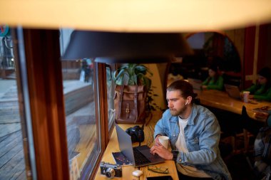 Kum ceketli yakışıklı beyaz adamın laptopta çalışan, odaklanmış bir portresi.