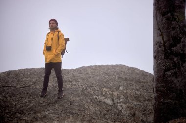 Dağın aşağısında, sisli havada yalnız yürüyen kameralı bir erkek.