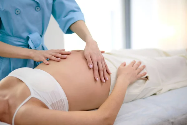 Przycięta fizjoterapeutka robi masaż brzucha pięknej ciężarnej kobiecie w spa — Zdjęcie stockowe