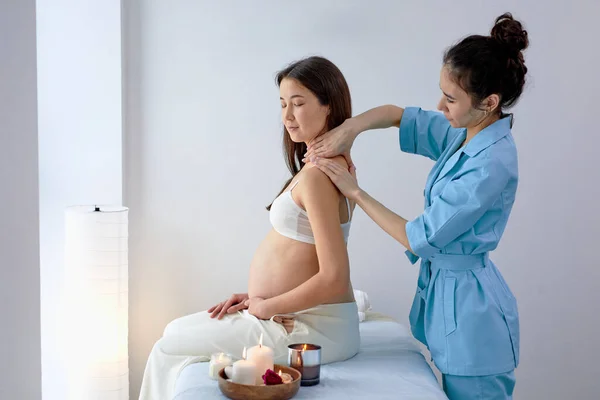 Vista lateral sobre fisioterapeuta femenina masajeando espalda y hombros de mujer embarazada —  Fotos de Stock
