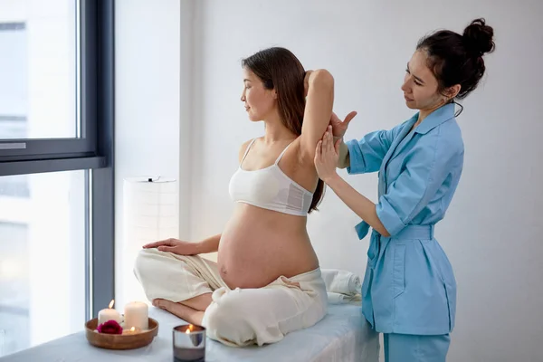 Agradable fisioterapeuta femenina masajeando espalda y hombros de mujer embarazada — Foto de Stock