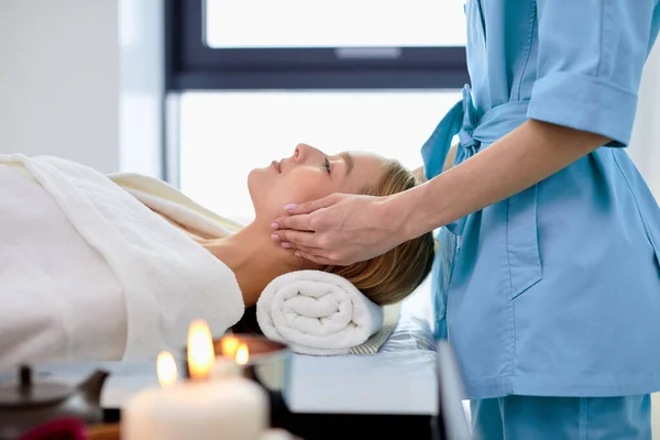 Jeune femme blonde recevant un massage du visage et de la tête au centre spa, vue latérale — Photo