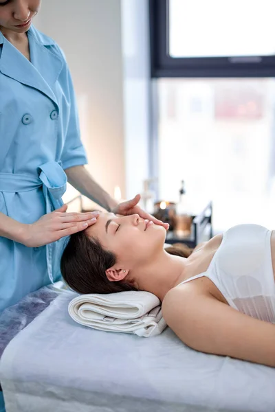 Massagem facial. Asiática jovem mulher recebendo tratamento de spa por massagista, vista lateral — Fotografia de Stock