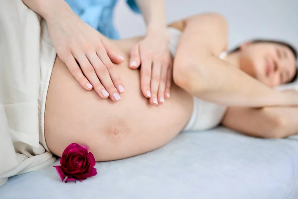 Masajista recortado haciendo masaje a mujer embarazada acostada en la cama —  Fotos de Stock