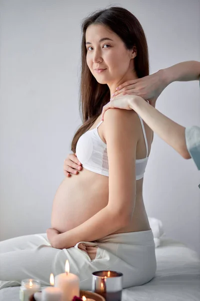Hamile Asyalı hoş bir kadın yatakta oturuyor ve doğum öncesi masaj yaptırıyor. — Stok fotoğraf