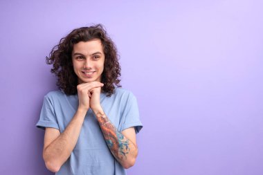 Mavi tişörtlü genç kıvırcık erkek, kurnaz bir ifadeyle, ellerini birarada tutarak geldi.