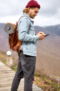 Akıllı telefon ve cep telefonu kullanan genç bir adamın yan görüş portresi. seyahat kavramı