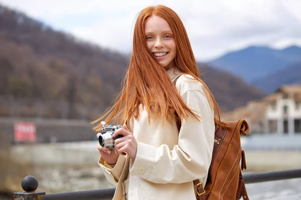 Glad rödhårig kvinna med retrokamera i händerna på resan, i bergen — Stockfoto