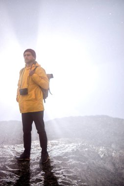 Dağın aşağısında sisli havada tek başına yürüyen kameralı bir erkek silueti.