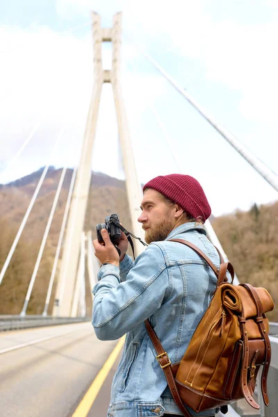 Fotógrafo hipster jovem andando na ponte na área urbana tirando foto na câmera — Fotografia de Stock