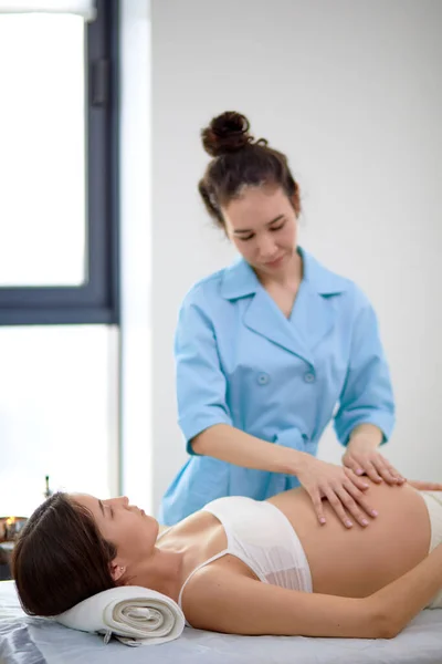 Mamá-a-ser recibir tratamiento osteopático en la clínica. terapeuta manipula vientre — Foto de Stock