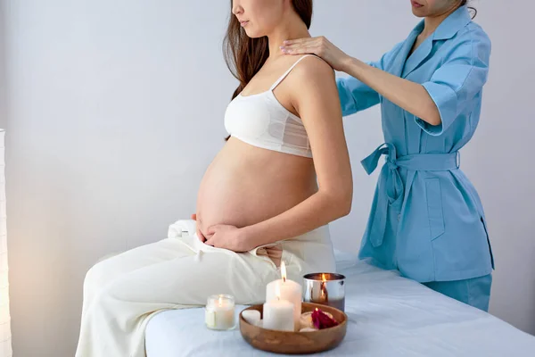 Masajista fisioterapeuta en uniforme azul masajeando espalda de mujer embarazada en spa — Foto de Stock