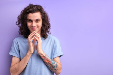 Sinsi, entrikacı, kıvırcık saçlı, tişörtlü, el ele tutuşan şeytani fikirli erkek portresi.