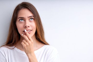 Beyaz stüdyo arka planında kameraya poz veren düşünceli beyaz kadın.