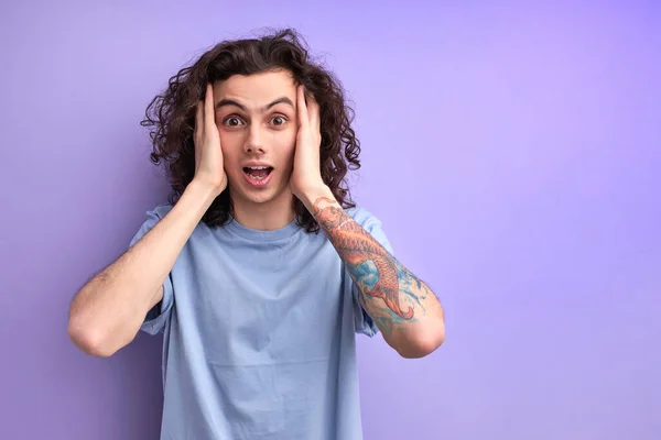 Jovem morena bonito homem com cabelo encaracolado é chocado, surpresa e expressão espantada com as mãos no rosto — Fotografia de Stock