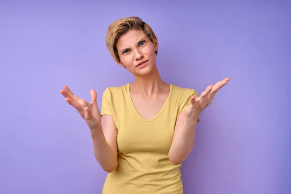What the fuck. Woman with short hair spreading arms, misunderstanding isolated on purple — стоковое фото