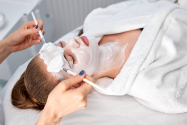 Genç ve güzel bir kadın kanepede uzanıyor kozmetik uzmanı tarafından tedavi ediliyor.