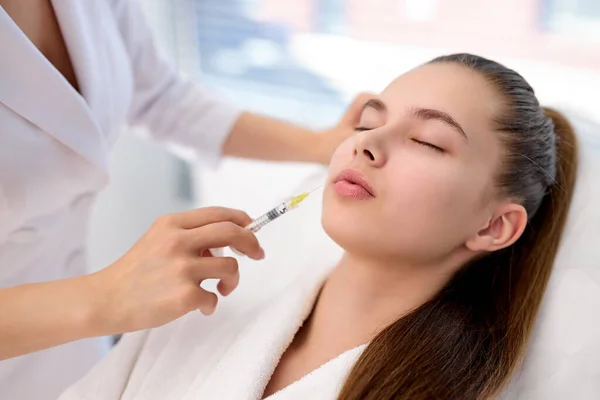 Жінка-косметолог робить ін'єкцію ботокса у жіночих губах, тримаючи шприц — стокове фото