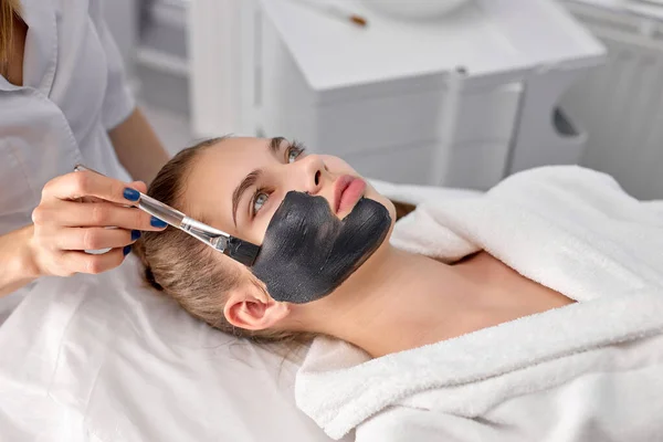 Le mani della donna cosmetologa caucasica che applica la maschera facciale sul viso dei clienti — Foto Stock