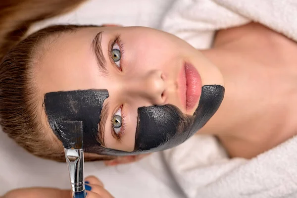 Eljárás alkalmazása fekete maszk arcán gyönyörű nő, felső nézet. Gyógykezelések — Stock Fotó