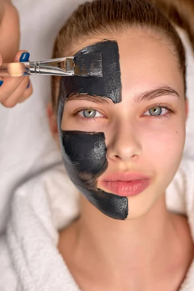 Draufsicht auf eine Frau mit schwarzer kosmetischer Gesichtsmaske, die im Wellnessbereich auf dem Bett liegt. Gesichtspeeling — Stockfoto