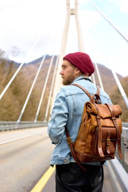 Köprüde tek başına yürüyen erkek turist. Yaşam tarzı, açık havada tatiller, deri sırt çantalı.