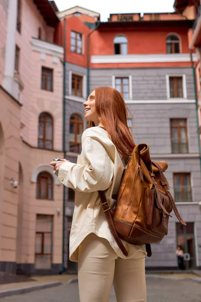 Bakifrån trendig ung rödhårig resenär kvinna med kamera stående i en urban gata — Stockfoto