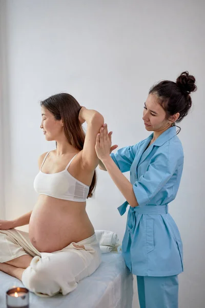 Фізіотерапевт масажиста у блакитній формі масажує вагітну жінку у курортному центрі. — стокове фото