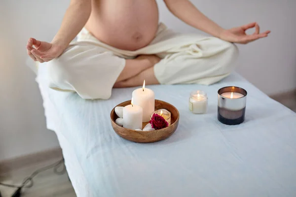 Обрізана молода вагітна жінка сидить у положенні йоги в спа-кімнаті, розслабляючись — стокове фото