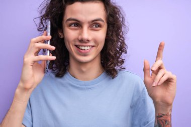 Bağlantı iyi. Kıvırcık hippi cep telefonuyla konuşuyor ve gülümsüyor, mor arka plan, kopyalama alanı