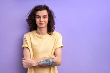 Kollarını kavuşturmuş gülümseyen genç bir erkek, kameraya özgüvenle bakıyor, boşluğu kopyalıyor.