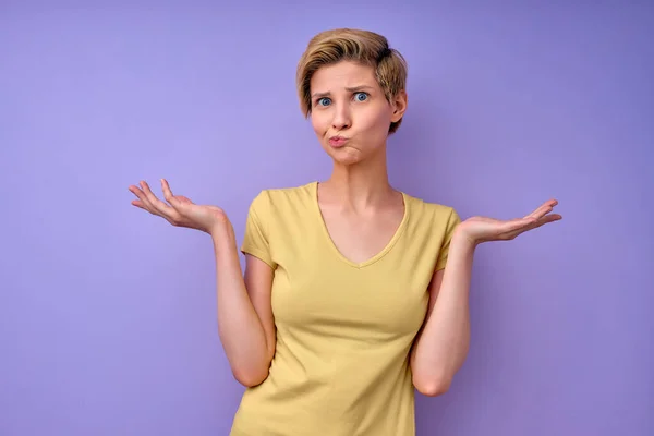 Clueless jonge Kaukasische vrouw met kort haar dragen geel tshirt tegen paars — Stockfoto