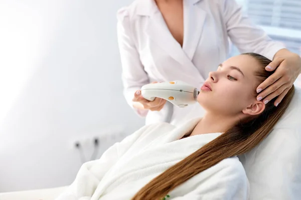 Bella femmina sdraiata nel salone termale ottenere massaggio per il viso con apparat professionale — Foto Stock