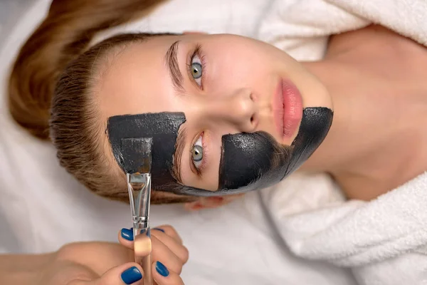 Top kilátás nő fekete kozmetikai maszk feküdt az ágyon spa. Archámlás — Stock Fotó
