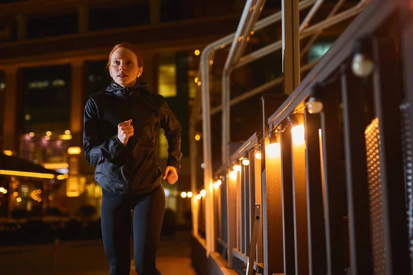 Atractiva Slim Fitness Mujer en Negro desgaste atlético está corriendo en la noche de la ciudad de la calle —  Fotos de Stock