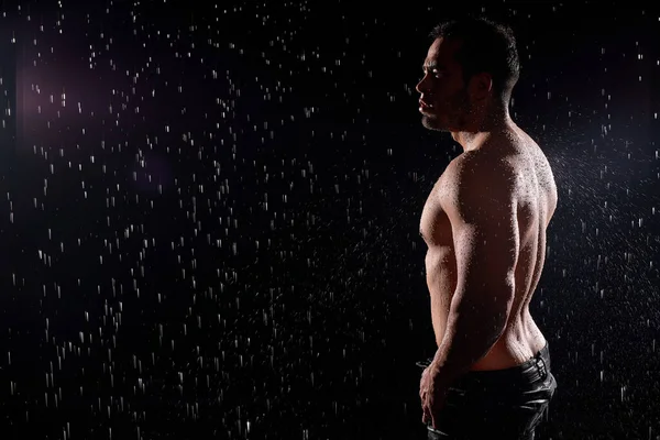 Guapo joven con el torso desnudo posando en la cámara sobre fondo negro. — Foto de Stock