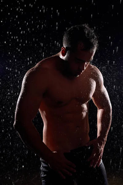 Superbe homme au corps musclé posant sous la pluie, avec torse nu, gouttes d'eau sur le corps — Photo