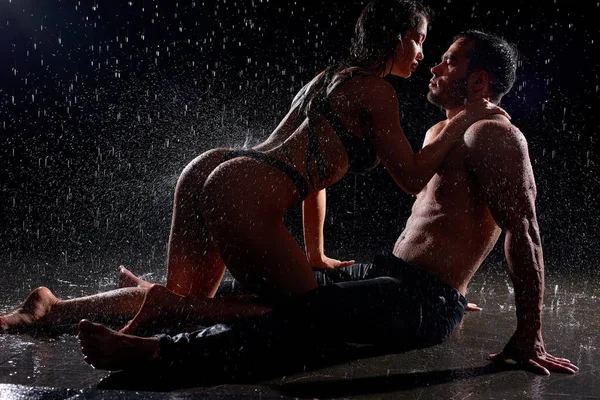 Man och kvinna innan sex, våt sexig kvinna kommer nära mannen sitter i regn, mörk studio Stockfoto