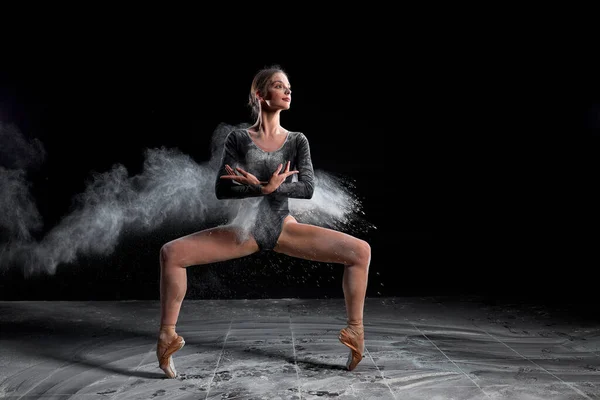 Mujer flexible bailando con harina sobre fondo negro en estudio, moviéndose con las piernas separadas — Foto de Stock