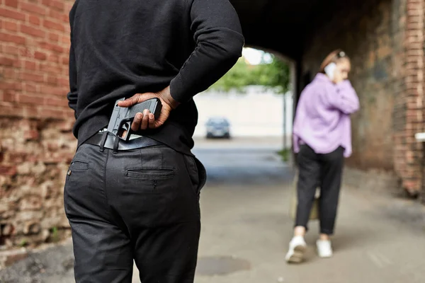 Vista trasera del hombre irreconocible que lleva un arma y sigue a la joven que camina —  Fotos de Stock