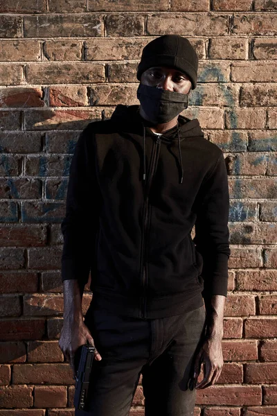 Maskeli Afrikalı Amerikalı haydut tuğla duvarın yanında duruyor, siyah giyen holigan. — Stok fotoğraf