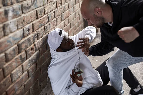 Vista lateral del bandido barbudo Hooligan exigiendo dinero a un extraño africano — Foto de Stock