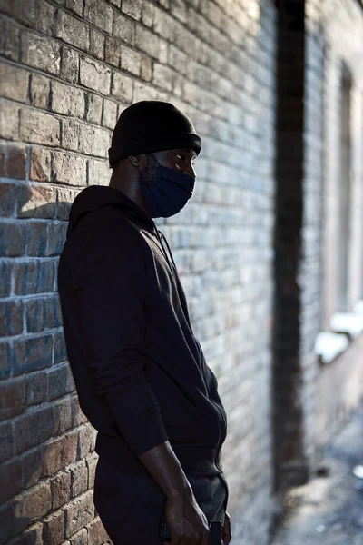Молодой африканский американец в черной маске, стоящий на улице в ожидании жертвы — стоковое фото